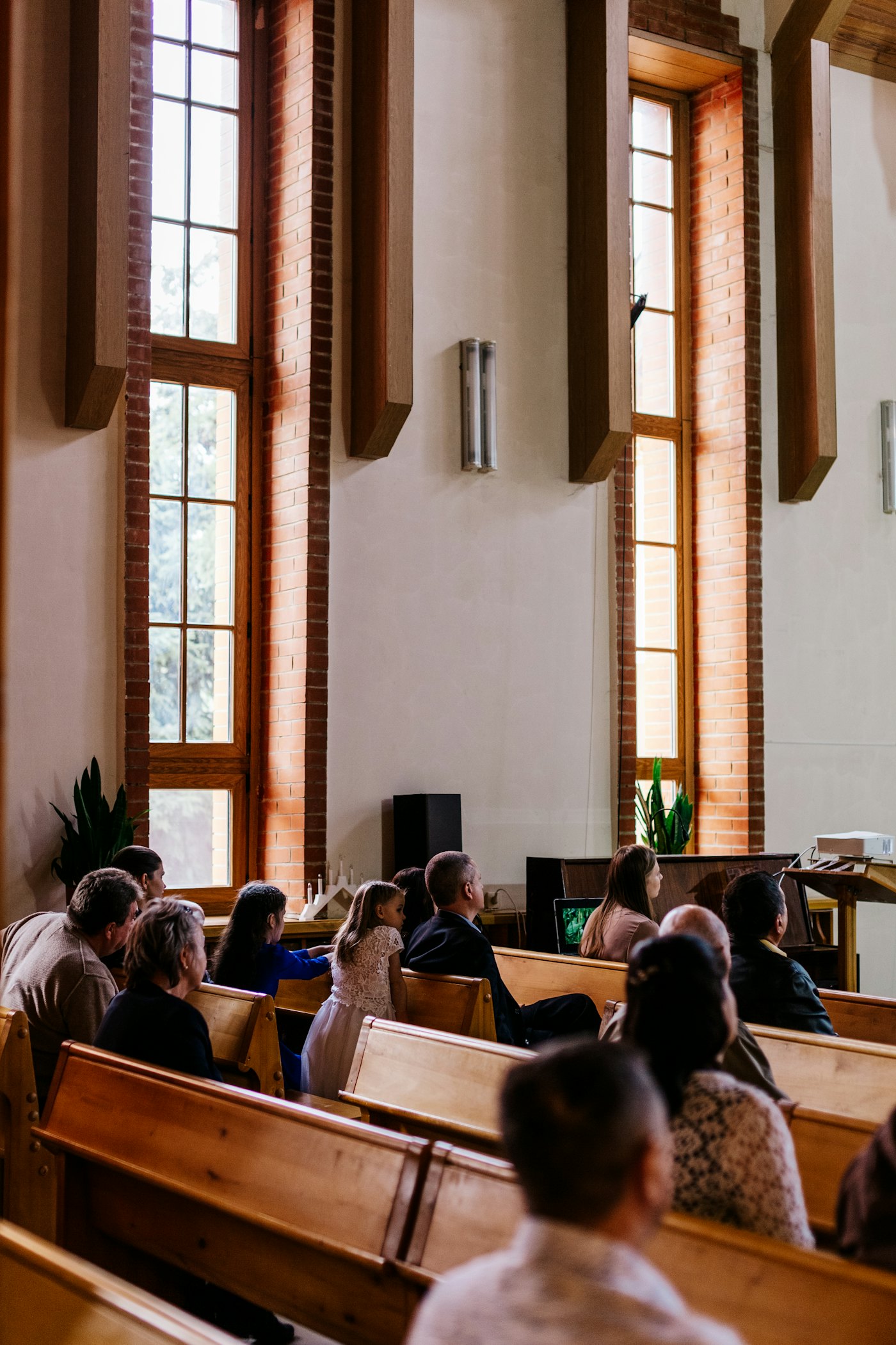 A congregation seated in wooden pews beside tall windows during a service
