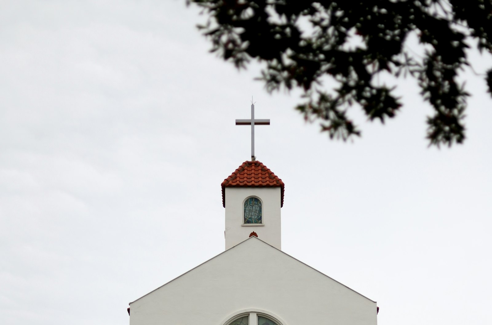 A white church steeple with a cross, framed by tree branches