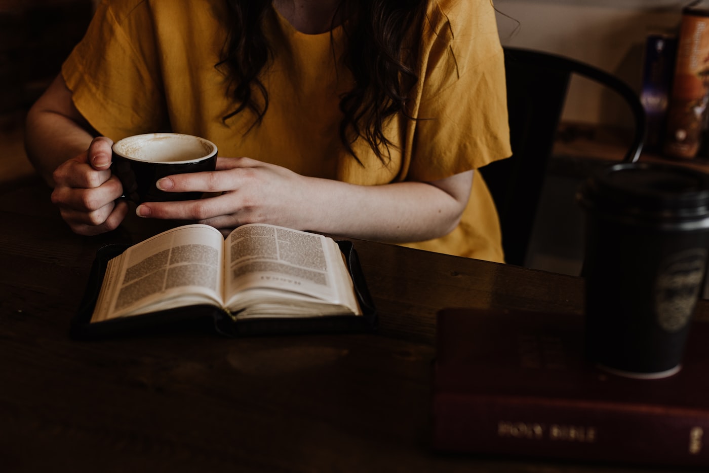 A woman holding a coffee cup at a table with an open Bible