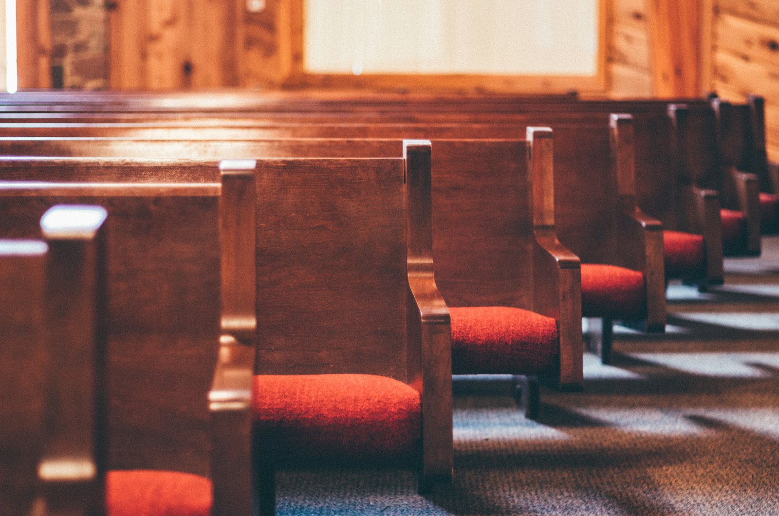Empty wooden church pews with red cushions in warm afternoon light