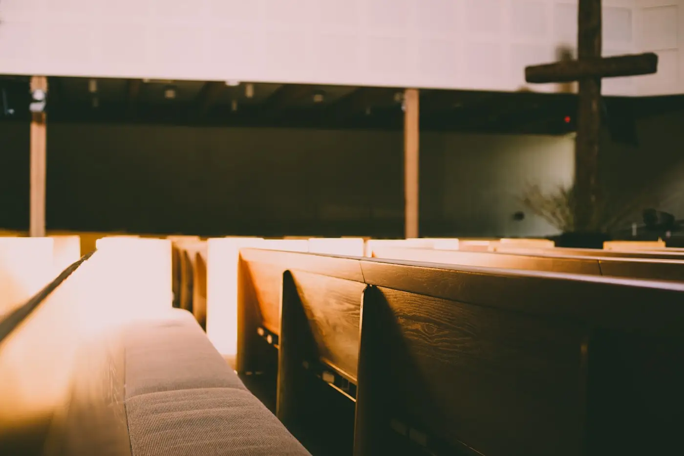 Empty church pews lit by warm evening light, with a wooden cross beyond